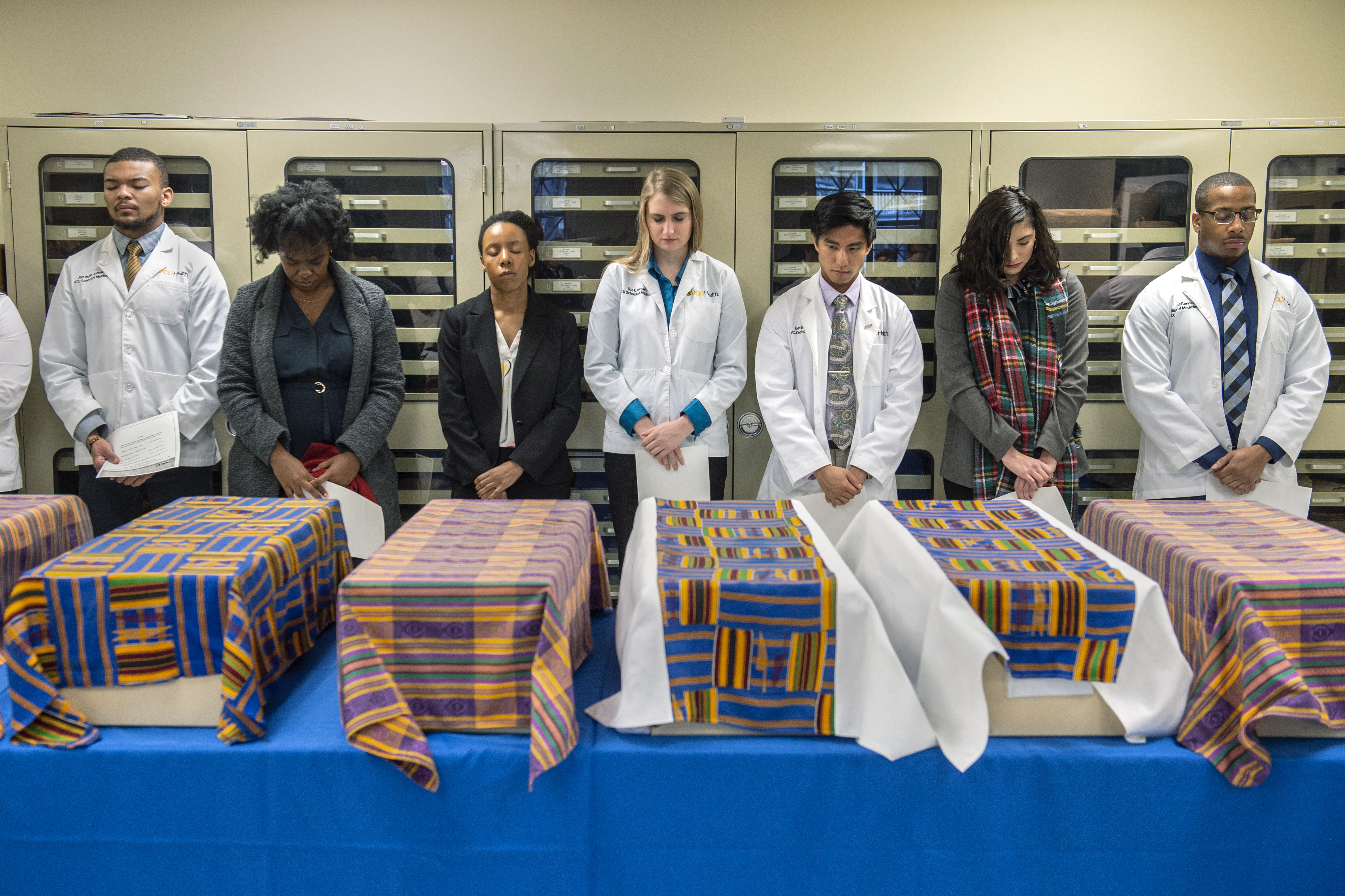 VCU Health Sciences students bow their heads in front of the ancestral remains of individuals recovered from the East Marshall Street Well during a prayer given by Del. Delores McQuinn. Nov. 25, 2019.